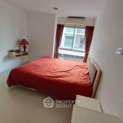 Cozy bedroom with red bedding and natural light from window, perfect for relaxation.