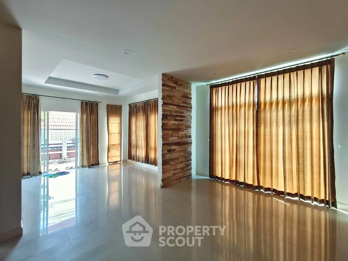 Spacious living room with large windows and elegant curtains, featuring a modern design and ample natural light.