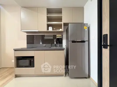 Modern kitchen with sleek cabinetry, microwave, and stainless steel fridge in a compact layout.