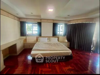 Spacious bedroom with wooden flooring and large windows in a modern apartment.