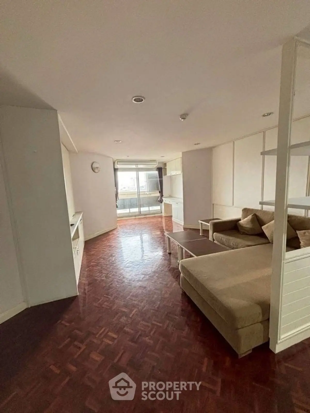 Spacious living room with parquet flooring and cozy sofa, leading to a bright balcony view.