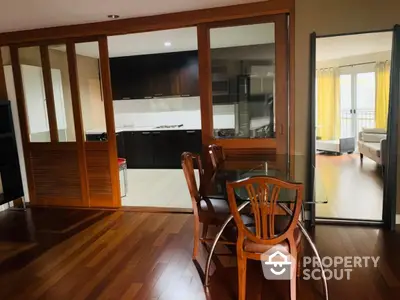 Spacious dining area with wooden flooring and glass table, adjacent to modern kitchen with sliding doors.