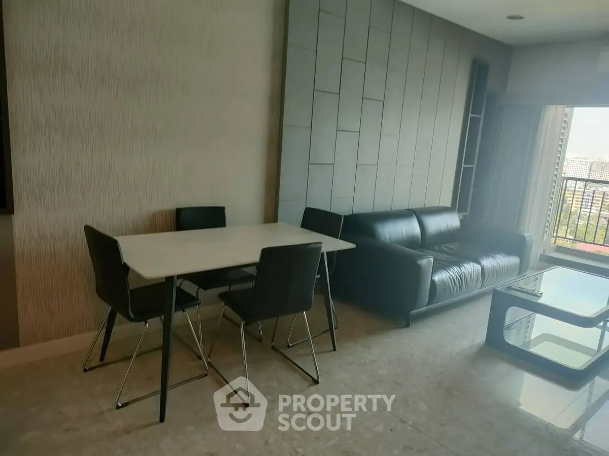 Modern living room with sleek black sofa and dining set, featuring a stylish balcony view.