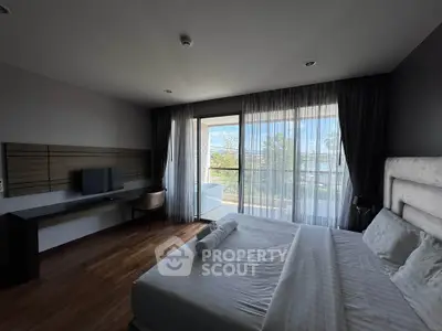 Spacious bedroom with large windows and balcony access, featuring modern furnishings and natural light.
