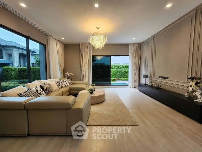 Luxurious living room with elegant chandelier and spacious seating area overlooking garden view.
