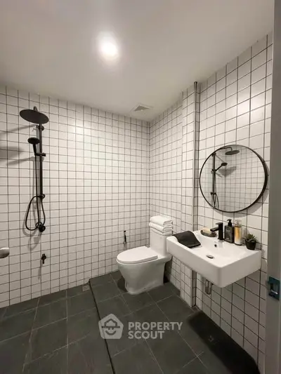 Modern bathroom with sleek design, featuring a round mirror, white tiles, and a rainfall showerhead.