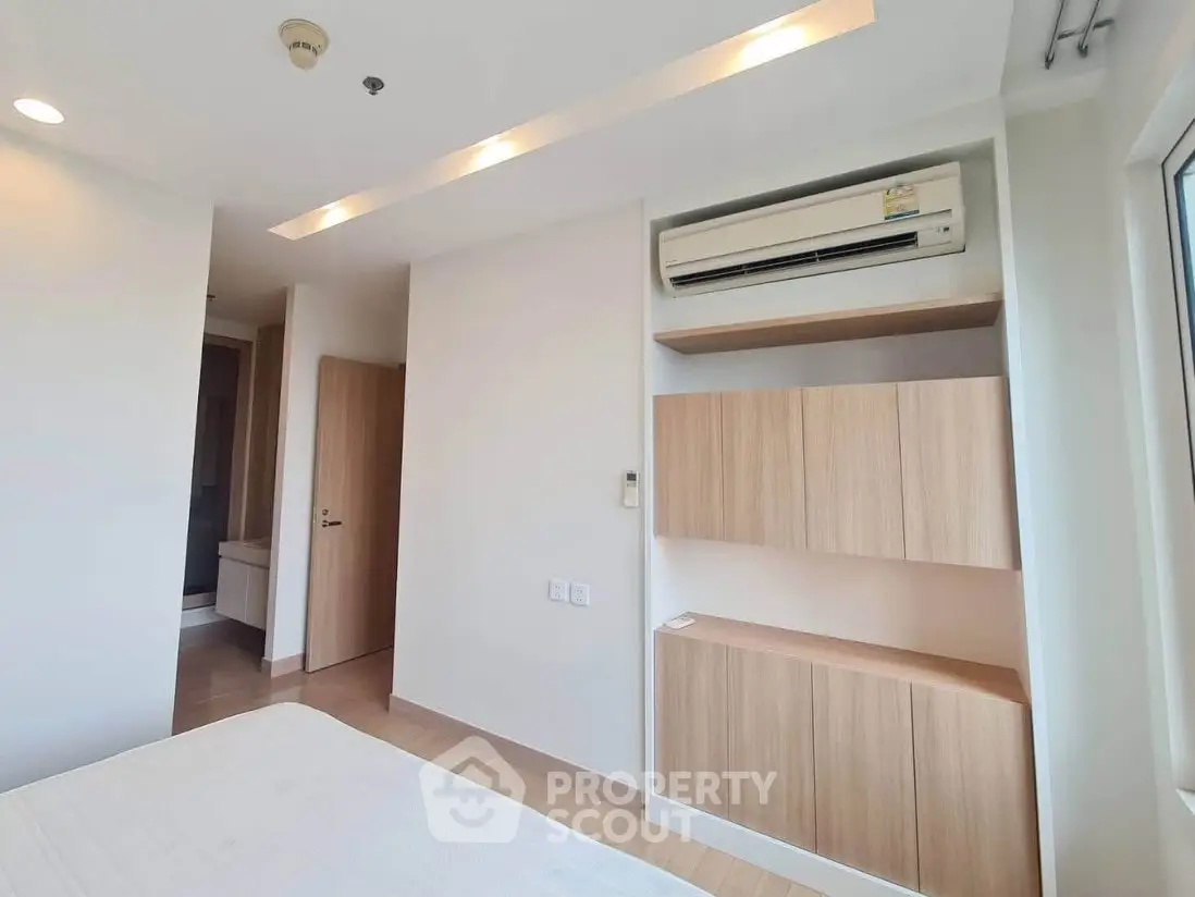 Modern bedroom with built-in wooden shelves and air conditioning unit, showcasing minimalist design.