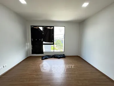 Spacious empty room with wooden flooring and large window.