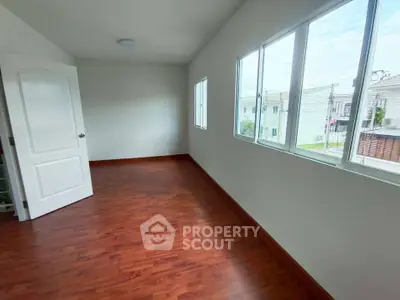 Spacious empty room with wooden flooring and large windows offering natural light.