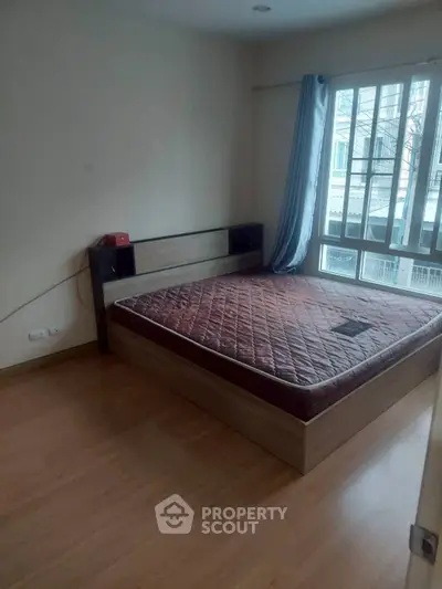 Cozy bedroom with large window and wooden flooring, perfect for relaxation.