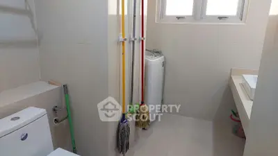 Compact bathroom with washing machine and cleaning tools, ideal for efficient space utilization.