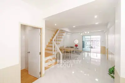 Spacious modern living room with staircase and dining area, featuring sleek white interiors and natural light.