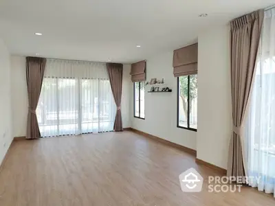 Spacious living room with elegant hardwood floors and ample natural light from large windows, complete with stylish drapery and serene neutral tones.