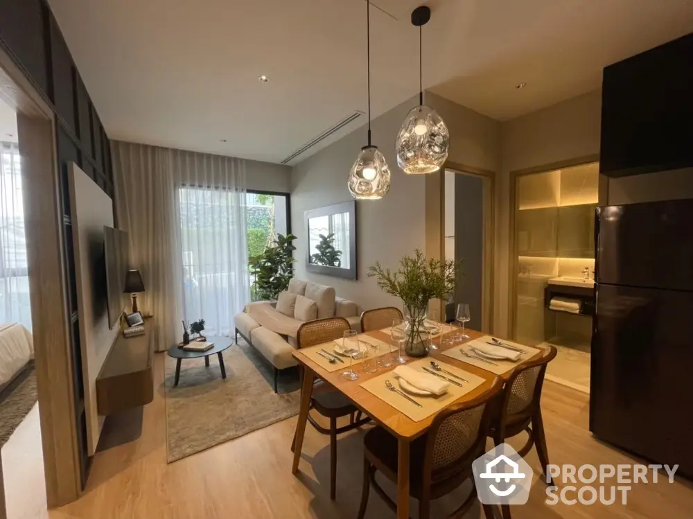 Elegant open-plan living space with modern furniture, chic pendant lights, and a seamless transition to a well-equipped kitchen, perfect for entertaining.