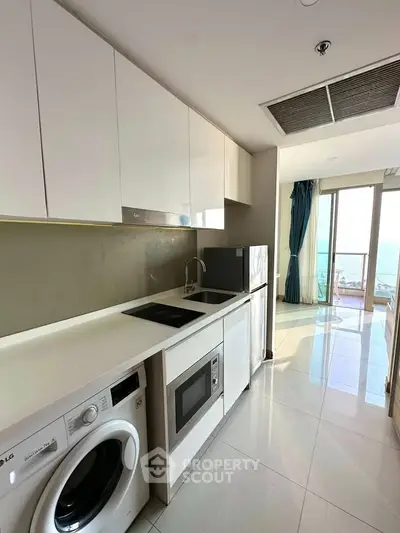 Modern kitchen with sleek appliances and open layout, featuring a washing machine and microwave.