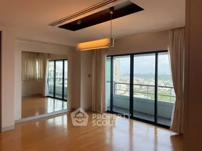 Spacious living room with large windows and balcony offering stunning city views.