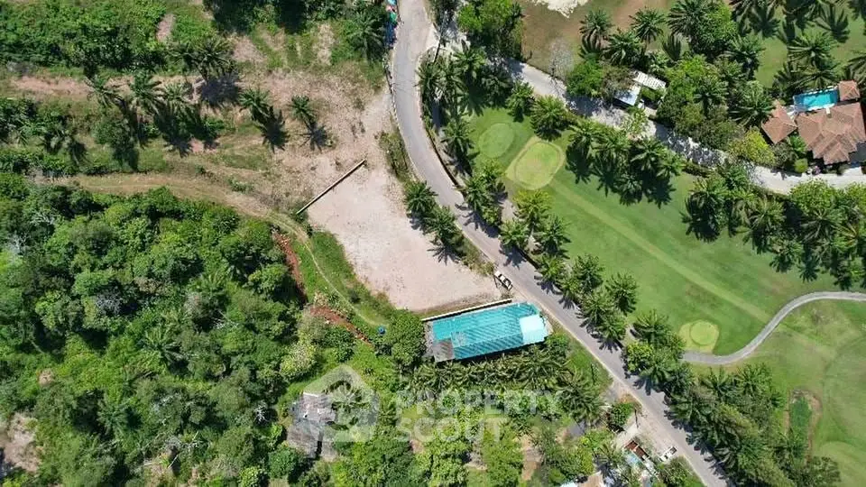 Aerial view of lush green landscape with golf course and palm trees, showcasing serene surroundings.