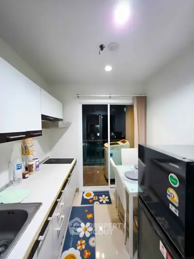 Modern kitchen with sleek cabinets and dining area, featuring a refrigerator and sliding glass doors.