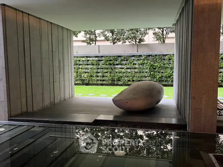 Modern architectural space with unique stone sculpture and lush greenery view.