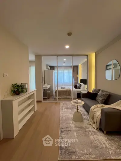 Modern living room with cozy sofa and stylish decor leading to a bright bedroom through glass doors.