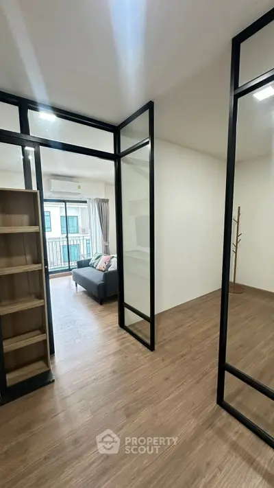 Modern apartment with open layout and balcony view, featuring sleek glass doors and wooden flooring.