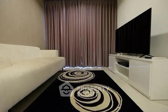 Modern living room with stylish sofa and large TV, featuring elegant curtains and a chic rug.