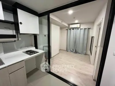 Modern studio apartment with sleek kitchen and spacious living area, featuring sliding glass doors and elegant flooring.