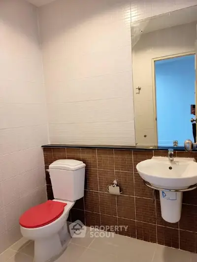 Modern bathroom with white tiles and red toilet seat in a real estate property.