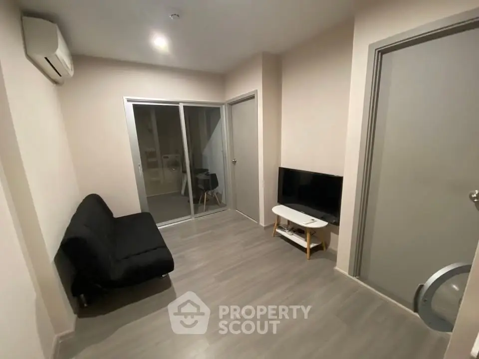 Modern living room with sleek flooring, compact sofa, and wall-mounted TV, perfect for cozy urban living.