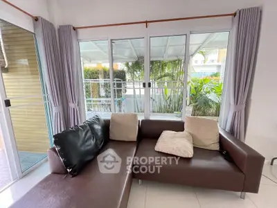 Spacious living room with large windows and garden view, featuring a modern L-shaped sofa.
