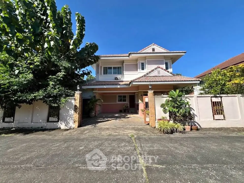 Charming two-story house with lush greenery and spacious driveway under clear blue sky.
