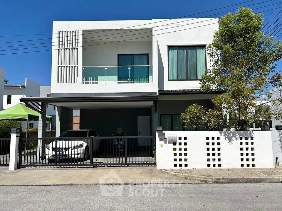 Modern two-story house with carport and balcony in a suburban neighborhood.