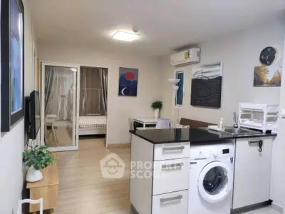 Modern open-plan living room with kitchen and washing machine, featuring stylish decor and natural light.
