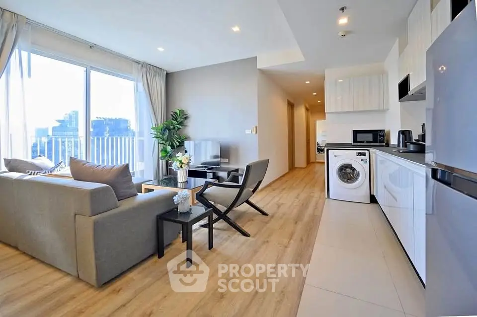 Modern open-plan living room with kitchen and washing machine, featuring sleek design and natural light.