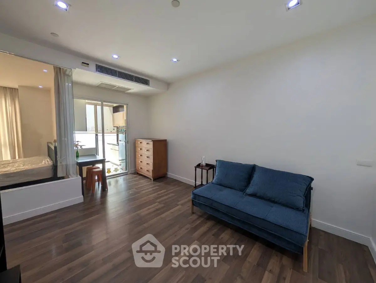 Modern living room with wooden flooring and blue sofa, adjacent to a balcony.