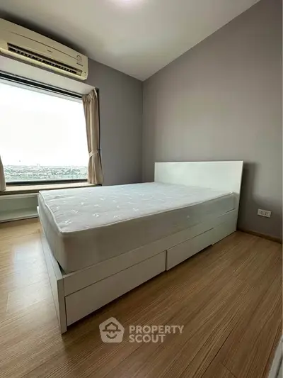 Modern bedroom with large window and air conditioning, featuring a sleek white bed and wooden flooring.