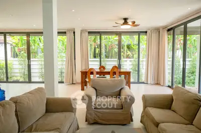 Spacious living room with cozy seating and large windows overlooking lush greenery.
