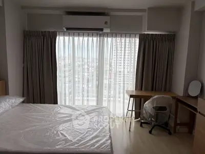 Spacious bedroom with city view, featuring a bed, desk, and large window with curtains.