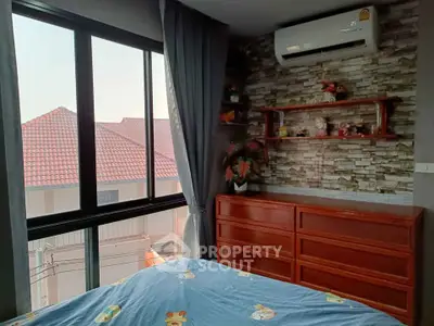 Cozy bedroom with large window and air conditioning, featuring decorative shelves and a view of neighboring rooftops.