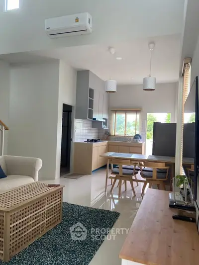 Modern open-plan living room with dining area and kitchen, featuring stylish furniture and natural light.