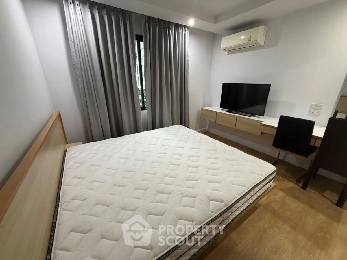 Modern bedroom with minimalist design, featuring a large bed, wall-mounted TV, and sleek furnishings.