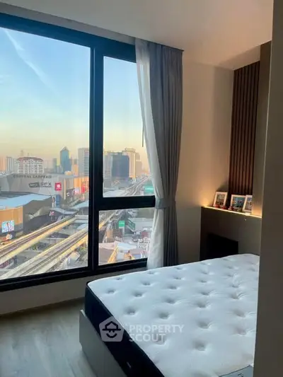 Modern bedroom with large window offering stunning city view at sunset.