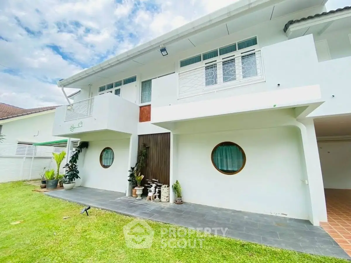 Charming white two-story house with lush green lawn and unique circular windows.