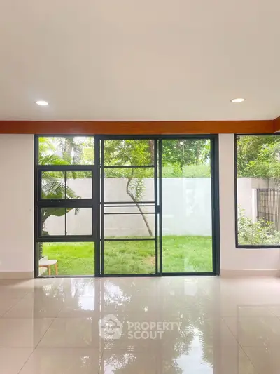 Spacious living room with large windows overlooking a lush garden, offering serene views and abundant natural light.