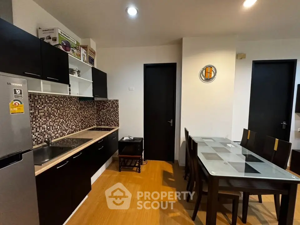 Modern kitchen with sleek black cabinets and dining area in contemporary apartment.