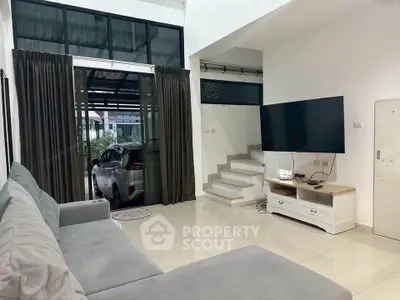 Spacious modern living room with large sofa and wall-mounted TV, featuring sleek tile flooring and natural light.