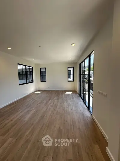 Spacious modern living room with large windows and wooden flooring, perfect for natural light lovers.
