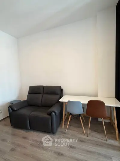 Modern living room with sleek black sofa and stylish dining set on wooden flooring.