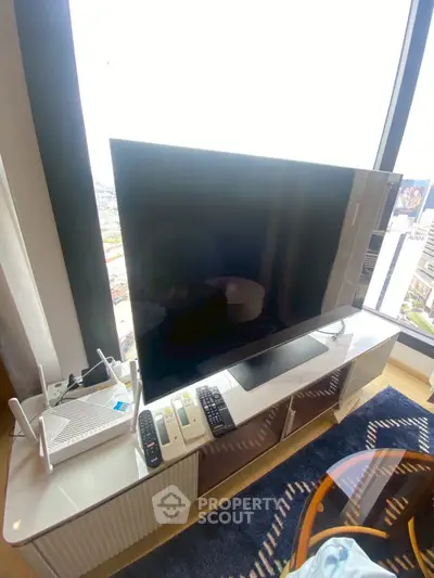 Modern living room with large TV and city view, featuring sleek furniture and natural light.