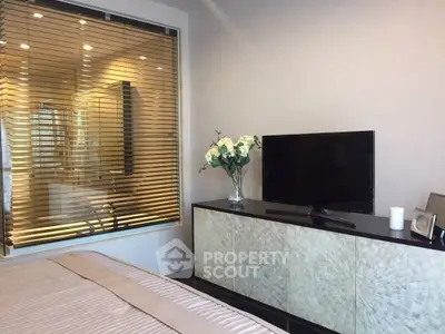 Modern bedroom with TV and elegant decor, featuring a window view into a luxurious bathroom.